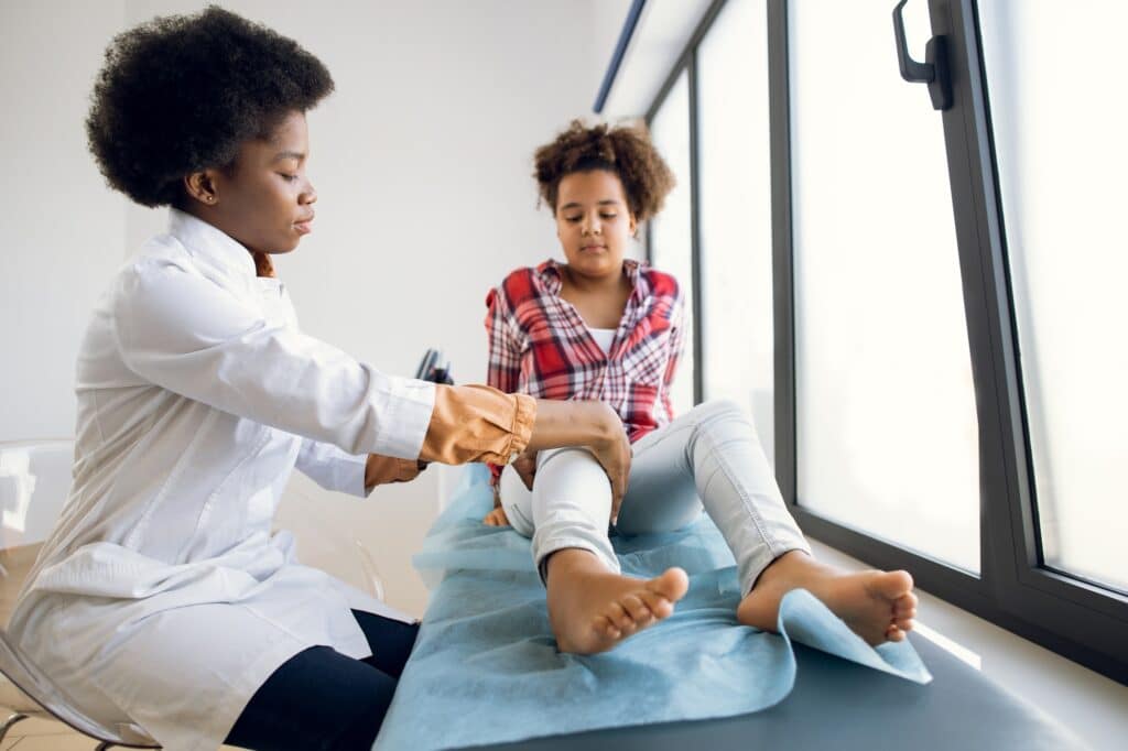 Post traumatic rehabilitation, sport physical therapy, osteopathy. Afro kid girl with a sore knee at